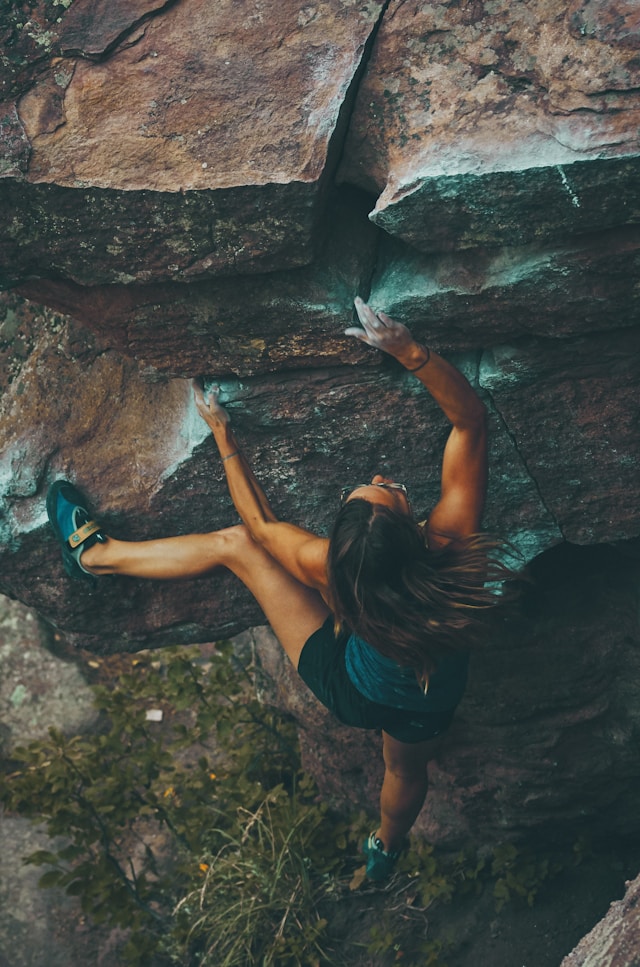 A woman in athletic clothes climbing up a cliff.